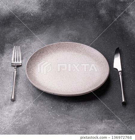 An empty round ceramic plate, knife, and fork as a dining table setting. An empty plate 136972768