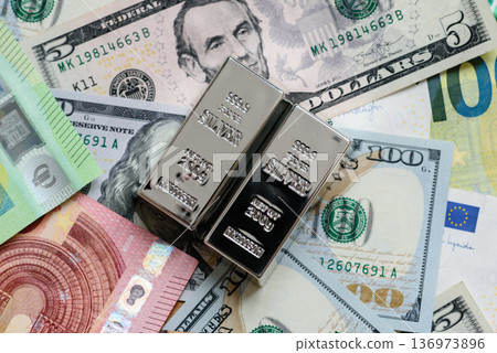 A silver bar, white metal against a backdrop of money, as a concept for the sales. A silver bar 136973896