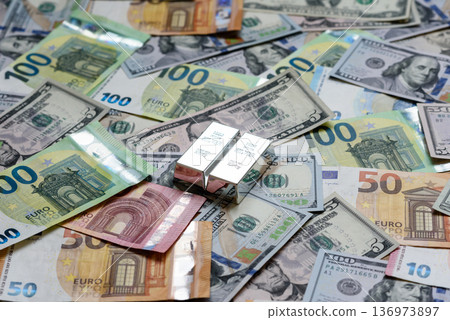 A silver bar, white metal against a backdrop of money, as a concept for the sales. A silver bar 136973897