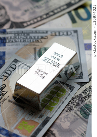 A silver bar, white metal against a backdrop of money, as a concept for the sales. A silver bar 136974023