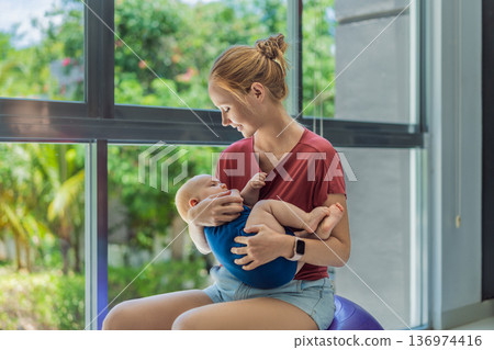 Young mother gently rocks her baby on a fitness ball at home, creating a calm loving atmosphere. Authentic family lifestyle, natural parenting and emotional bonding. Motherhood, wellbeing and baby Young mother gently rocks her baby on a fitness ball at home, creating a calm loving atmosphere. Authentic family lifestyle, natural parenting and emotional bonding. Motherhood, wellbeing and baby 136974416