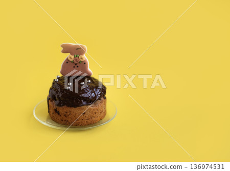 Easter cake decorated with glossy chocolate glaze and bunny figurine on bright yellow background, festive spring composition with copy space for text Easter cake decorated with glossy chocolate glaze and bunny figurine on bright yellow background, festive spring composition with copy space for text 136974531