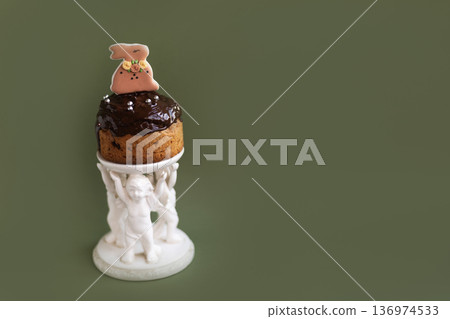 Easter cake decorated with chocolate and bunny figurine placed on ceramic stand with angel details, elegant holiday presentation 136974533