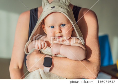 Mother holding her baby wrapped in a soft towel after bath at home, sharing a warm caring moment. Authentic parenthood scene showing love, safety and comfort. Baby hygiene, wellbeing and family Mother holding her baby wrapped in a soft towel after bath at home, sharing a warm caring moment. Authentic parenthood scene showing love, safety and comfort. Baby hygiene, wellbeing and family 136974632