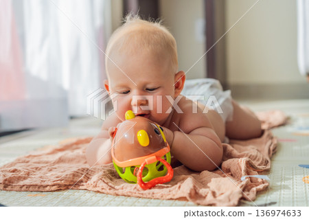 Little baby playing with toys on a soft baby play mat at home. Early childhood development, sensory play, learning through play, curiosity, and happy infant activity concept for modern parenting. 136974633