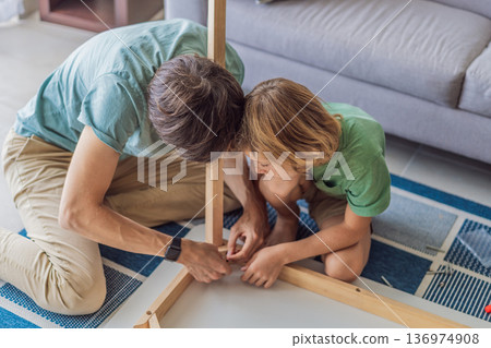 Father and his son assembling a table together in the living room at home. Meaningful family moment showing teamwork, learning and support. Fatherhood, home improvement and bonding through shared Father and his son assembling a table together in the living room at home. Meaningful family moment showing teamwork, learning and support. Fatherhood, home improvement and bonding through shared 136974908