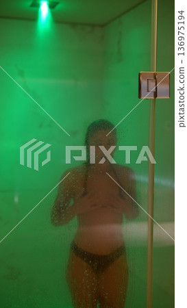 Peaceful woman standing amid soft emerald glow with dewy skin 136975194