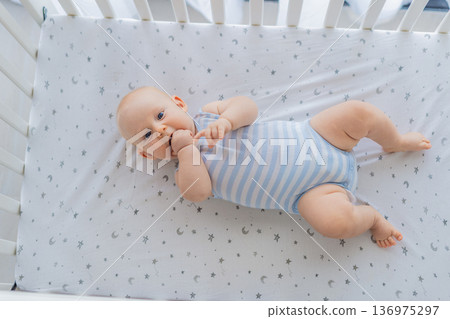 Baby lying peacefully in a cozy crib at home, feeling safe and calm in a warm nursery atmosphere. Simple everyday moment of care and comfort. Infant sleep, early childhood and gentle parenting concept 136975297