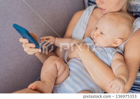 Baby sitting on mother lap while she looks at her smartphone, emotionally disconnected. Symbolic scene showing impact of screen distraction on infants and unmet emotional needs. Digital parenting and Baby sitting on mother lap while she looks at her smartphone, emotionally disconnected. Symbolic scene showing impact of screen distraction on infants and unmet emotional needs. Digital parenting and 136975353