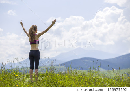 Slim young woman with raised arms outdoors on background of beautiful mountain landscape on sunny summer day. Slim young woman with raised arms outdoors on background of beautiful mountain landscape on sunny summer day. 136975592