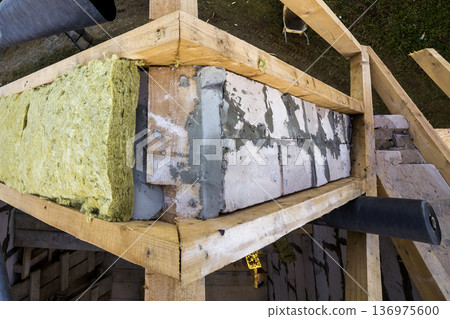 Roof construction and insulation with mineral wool. Wooden beams frame on walls of hollow foam insulation blocks. Roofing underlayment, water-resistant waterproof barrier material as protection. Roof construction and insulation with mineral wool. Wooden beams frame on walls of hollow foam insulation blocks. Roofing underlayment, water-resistant waterproof barrier material as protection. 136975600