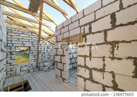 House interior under construction and renovation. Energy saving walls of hollow foam insulation blocks and bricks, ceiling beams and roof frame. House interior under construction and renovation. Energy saving walls of hollow foam insulation blocks and bricks, ceiling beams and roof frame. 136975603