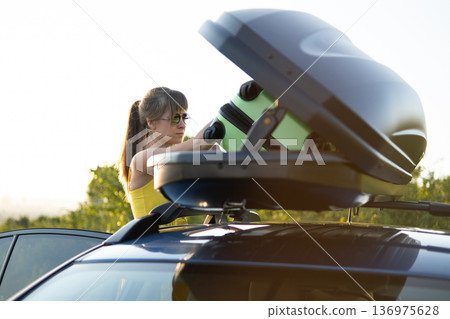 Young woman taking green suitcase from car roof rack. Travel and vacations concept. Young woman taking green suitcase from car roof rack. Travel and vacations concept. 136975628