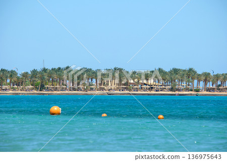 Yellow buoys floating on sea surface as marker for swimming restriction in deep water at tropical resort with view of coast line in distance. Human life safety concept. 136975643