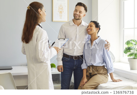 Smiling happy young couple sitting with female family doctor therapist in medical clinic. 136976738