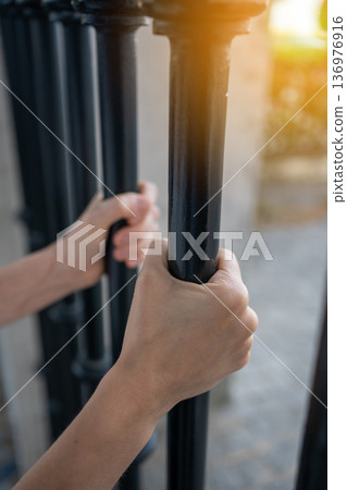 Closeup of hands gripping metal gate bars during Closeup of hands gripping metal gate bars during 136976916
