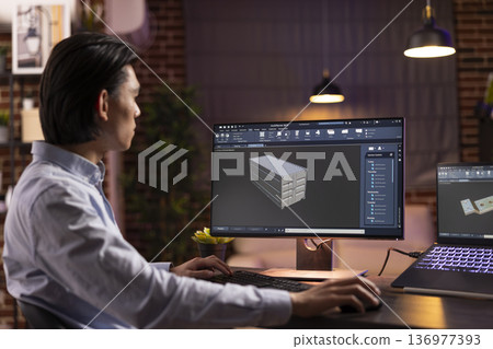 Male freelancer focusing on CAD software, creating precise 3D model structures from apartment during evening hours. Young asian man developing online industrial tools using computer and laptop setup. Male freelancer focusing on CAD software, creating precise 3D model structures from apartment during evening hours. Young asian man developing online industrial tools using computer and laptop setup. 136977393