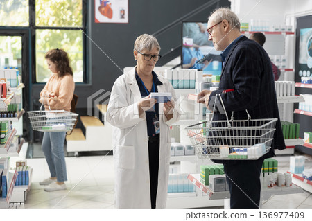 Female medical specialist supports senior client by reviewing supplements and healthcare items. The calm discussion near pharmacy shelves reflects responsible guidance in professional retail drugstore Female medical specialist supports senior client by reviewing supplements and healthcare items. The calm discussion near pharmacy shelves reflects responsible guidance in professional retail drugstore 136977409