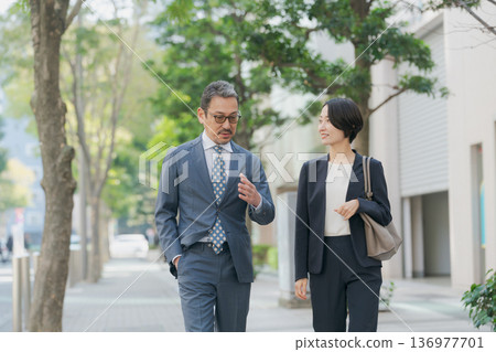 身著西裝的男女邊走邊聊 身著西裝的男女邊走邊聊 136977701