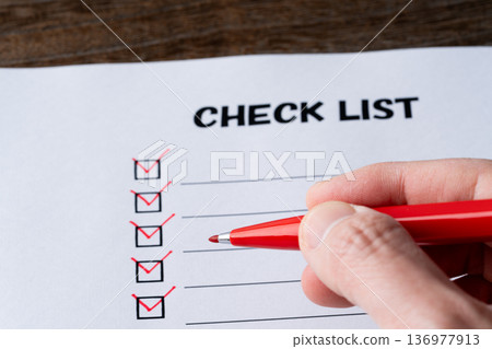 特寫鏡頭：一手用紅筆在清單紙上勾選項目。 136977913