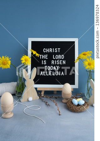 CHRIST THE LORD IS RISEN TODAY ALLELUIA text on letter board with bunny wooden figures eggs and fresh flowers. Easter composition content still life. Christian symbols of spring 136978324