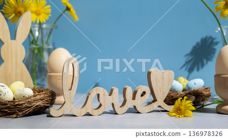 Wooden word LOVE traditional greeting to christian holiday. Festive mood composition with bunnies and yellow flowers on pastel blue background. Sustainable natural materials 136978326