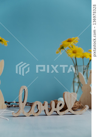 LOVE wooden word on festive blue background and eco-friendly zero waste natural decoration. Yellow daisies flowers. Bunny egg. Holiday greeting LOVE wooden word on festive blue background and eco-friendly zero waste natural decoration. Yellow daisies flowers. Bunny egg. Holiday greeting 136978328
