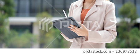 Young caucasian businesswoman writing on digital tablet in city. 136978538