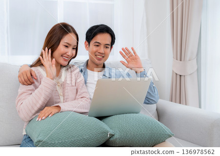 Happy asian couple video call on laptop together in living room at home. Happy asian couple video call on laptop together in living room at home. 136978562