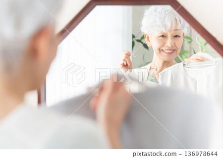 Senior woman choosing clothes in front of a mirror Senior woman choosing clothes in front of a mirror 136978644