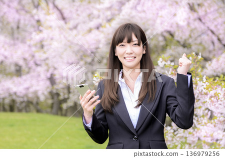 A woman in a suit pumping her fist in front of cherry blossoms 136979256