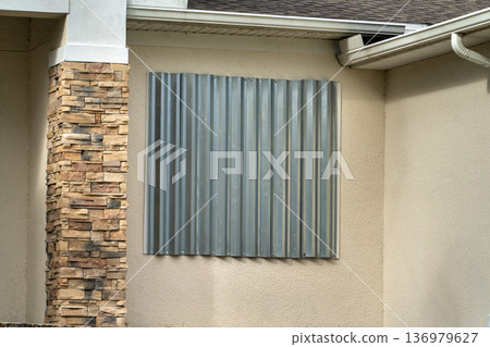 Steel sheets mounted as storm shutters for hurricane protection of house windows. Protective measures before natural disaster in Florida Steel sheets mounted as storm shutters for hurricane protection of house windows. Protective measures before natural disaster in Florida 136979627