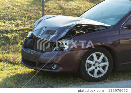 Crashed and dented car parked along a residential street near homes after a traffic accident. Traffic safety and accident aftermath concept. 136979652