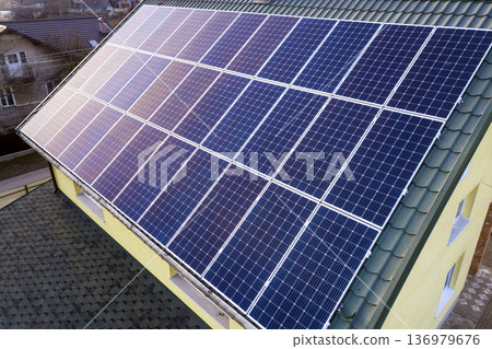 Aerial top view of new modern residential house cottage with blue shiny solar photo voltaic panels system on roof. Renewable ecological green energy production concept. Aerial top view of new modern residential house cottage with blue shiny solar photo voltaic panels system on roof. Renewable ecological green energy production concept. 136979676