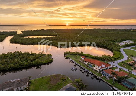 Sunset aerial view of American dream waterfront homes in Florida. Wealthy suburban neighborhood with palm trees and tropical design. Sunset aerial view of American dream waterfront homes in Florida. Wealthy suburban neighborhood with palm trees and tropical design. 136979710