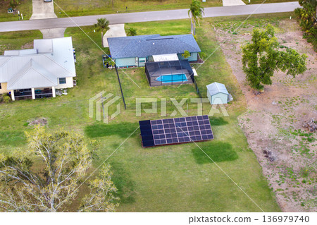 Private home with solar photovoltaic panels mounted on stand-alone frame on backyard ground for generating of clean ecological electric energy in suburban rural town area. Concept of autonomous house 136979740