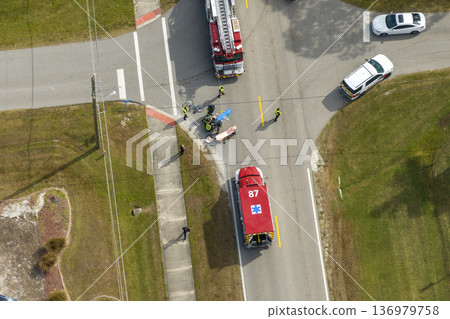 Victim of car accident on medical stretcher. First responders responding to car hit cyclist on street. Emergency medical technicians helping person of vehicle hitting pedestrian on road in USA 136979758