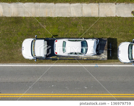 Tow truck hauling damaged car in traffic accident from crash site on American road 136979759