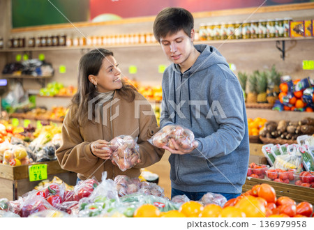 Young couple choosing onions in plastic bags in large grocery store Young couple choosing onions in plastic bags in large grocery store 136979958