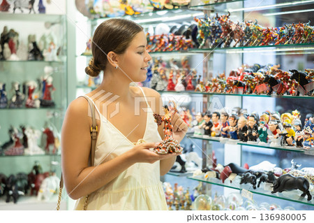 Female buyer holds in hands tests figurine she-dancer flamenco in memorable gifts shop Female buyer holds in hands tests figurine she-dancer flamenco in memorable gifts shop 136980005