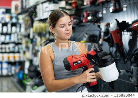 Woman choose examines spray gun airbrush in tools department of construction store 136980044