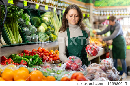 Saleswoman fills grocery store window with ripe bell peppers 136980045