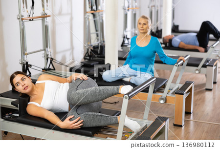 Young female in activewear lying on her side and stretching her leg forward for strengthening exercise on Pilates bed Young female in activewear lying on her side and stretching her leg forward for strengthening exercise on Pilates bed 136980112