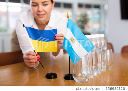 Employee of delegation prepares negotiating table - sets up flag of Ukrain and Argentine Employee of delegation prepares negotiating table - sets up flag of Ukrain and Argentine 136980120