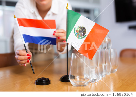 Unrecognizable girl sets midget flags of Mexico and Netherlands before international negotiations 136980164