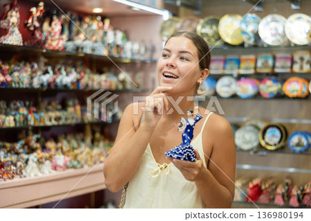 Female buyer holds in hands tests figurine she-dancer flamenco in memorable gifts shop Female buyer holds in hands tests figurine she-dancer flamenco in memorable gifts shop 136980194