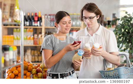 In shop youth girl and guy scan QR code and take reading sauce package bottle using phone camera In shop youth girl and guy scan QR code and take reading sauce package bottle using phone camera 136980197