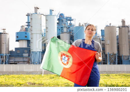 Sad young woman worker with flag of Portugal against background of factory Sad young woman worker with flag of Portugal against background of factory 136980201