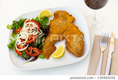 Portion of breaded cutlet, milanesa, with salad served on table 136980208