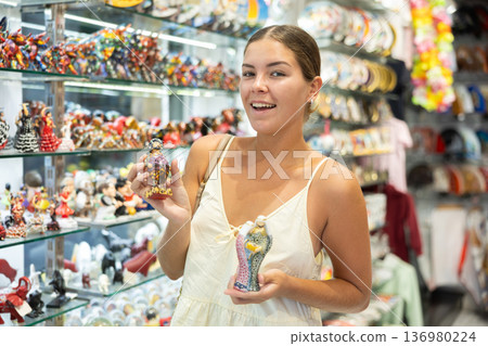 Female tourist happily chooses various souvenir figurines in spanish souvenir shop 136980224